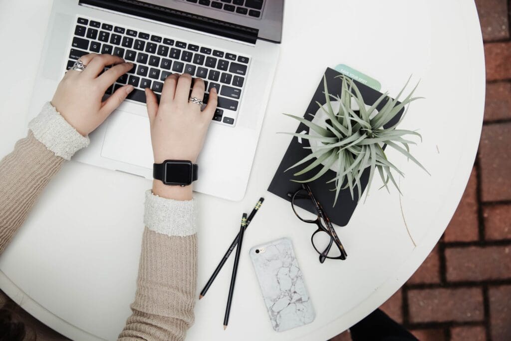 Birdseye view of a woman typing on a desk with a plant and glasses