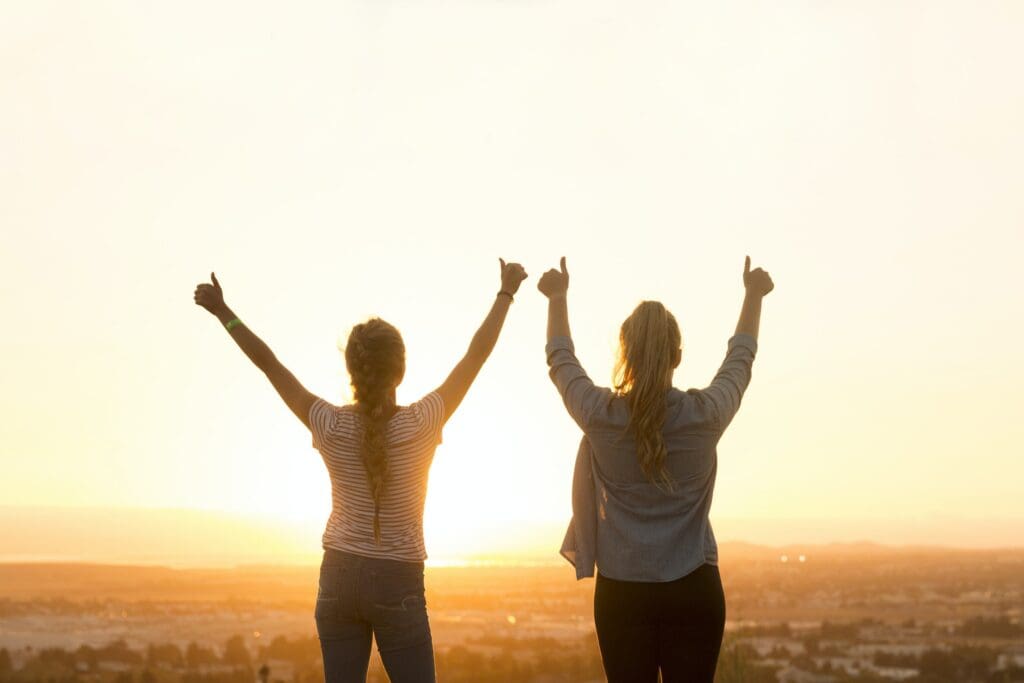 Two women cheering with their thumbs up looking out at scenery