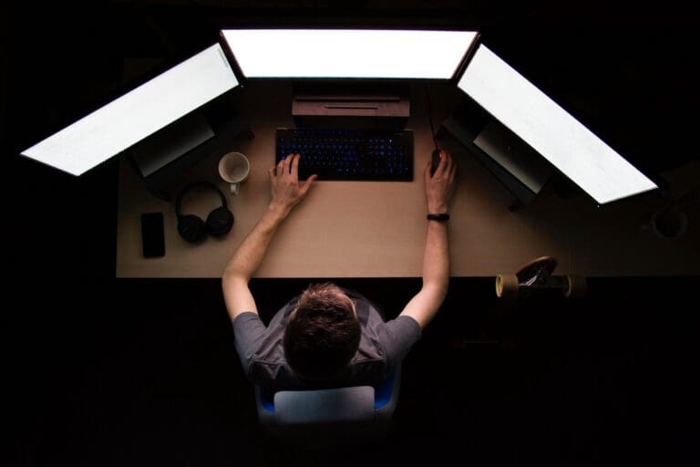 Birdseye view of a software developer looking at three computer screens on his desk