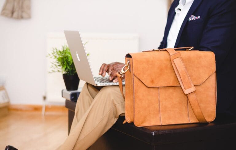 Man in the banking industry, wearing a suit working on a laptop with a brown leather bag next to him