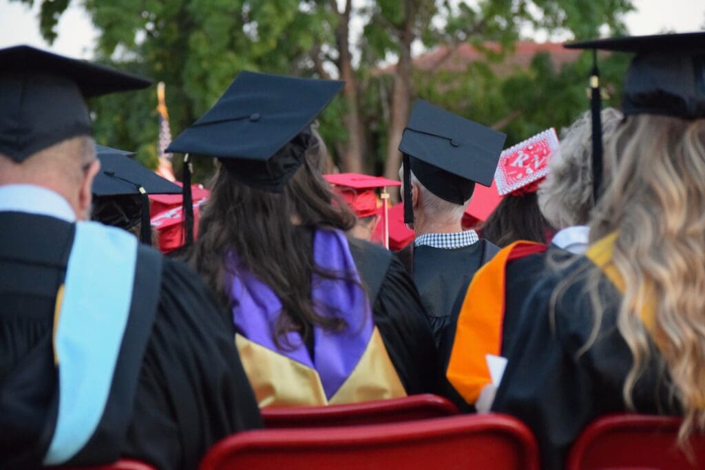 Looking at the back of a group of graduates' heads, wearing a cap and gown, graduation ceremony