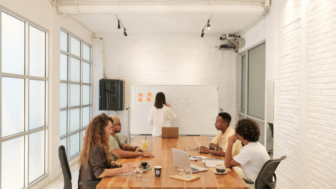 Diverse group of employees in a meeting room focused on a whiteboard, diversity in tech