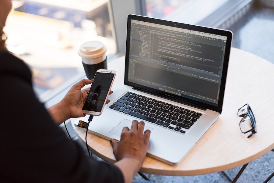 Woman coding app on laptop and testing on smartphone