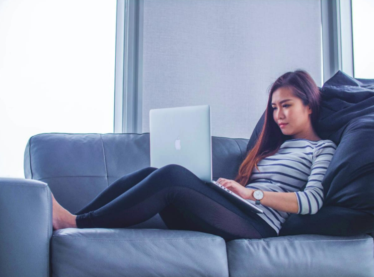 Woman on sofa looking for tech job on her laptop