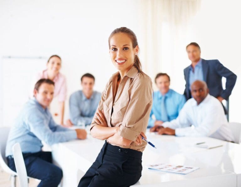 Female leader leans on table in front of team of colleagues