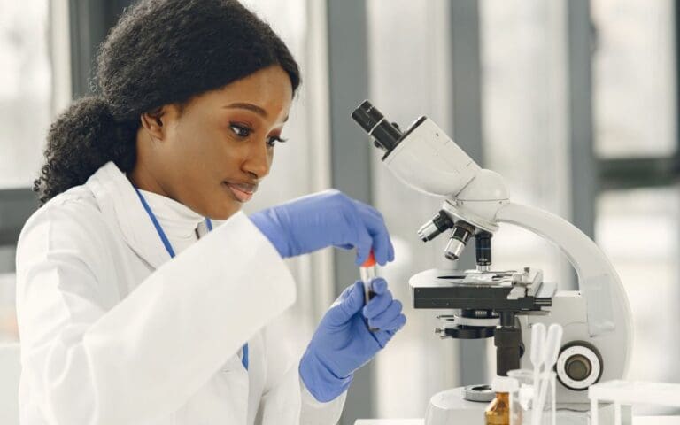 Black female scientist wearing a white lab coat looking at a microscope