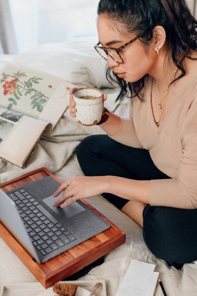 Woman drinks coffee sitting cross legged at laptop