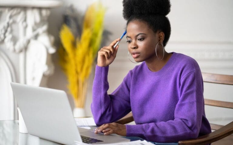 Black woman wearing a purple sweatshirt looking at a laptop, tech terms concept