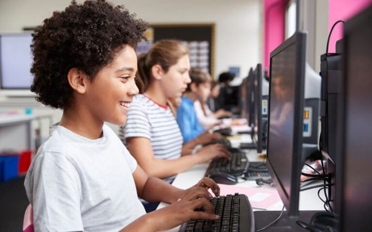 Young black girl in an IT lesson looking at a computer monitor with other female students