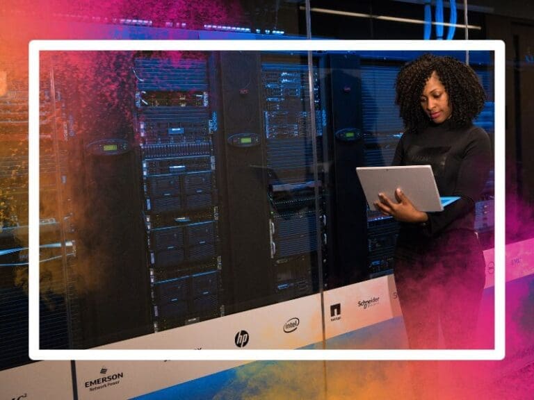 Female software engineer standing beside server racks holding a laptop