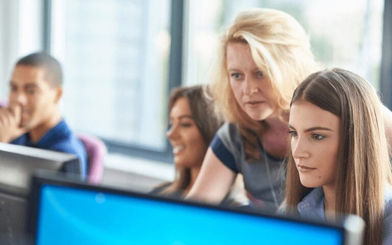 Female technology teacher looking over the shoulder of a female student using a computer