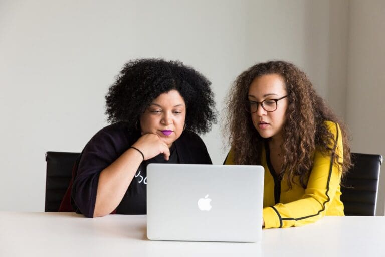 Two women looking at a laptop on a desk in a mentoring session, mentoring programmes for women