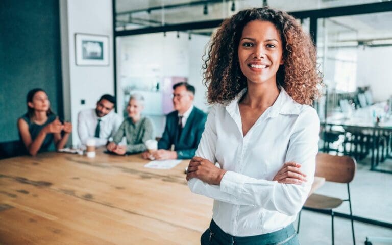 Photo of an African-American businesswoman with her arms crossed standing in front of her team, female leadership concept