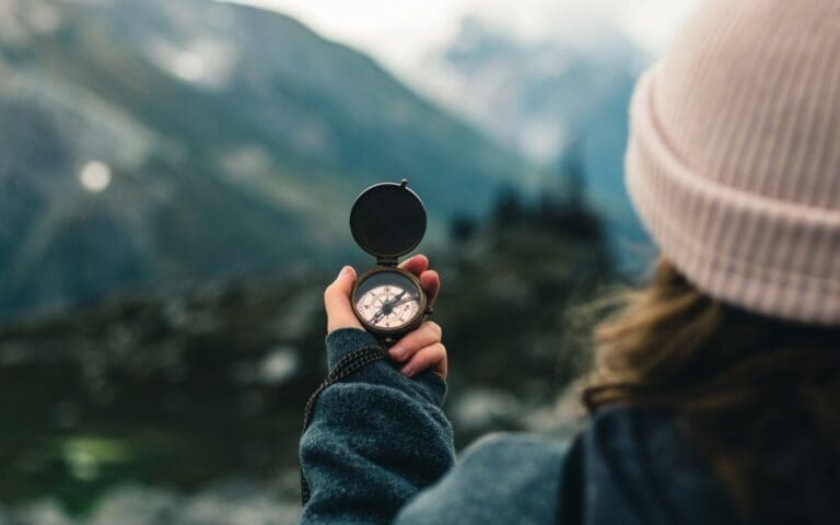 Woman wearing a pink woolly hat holding a compass while hiking