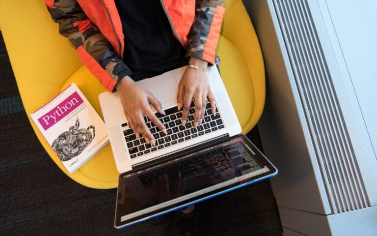 Person Using Macbook Pro, with a book on Python coding