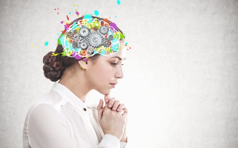 Side view of a pensive young woman with dark hair wearing a white blouse with a colourful brain full of cogs, neurodiverse women concept