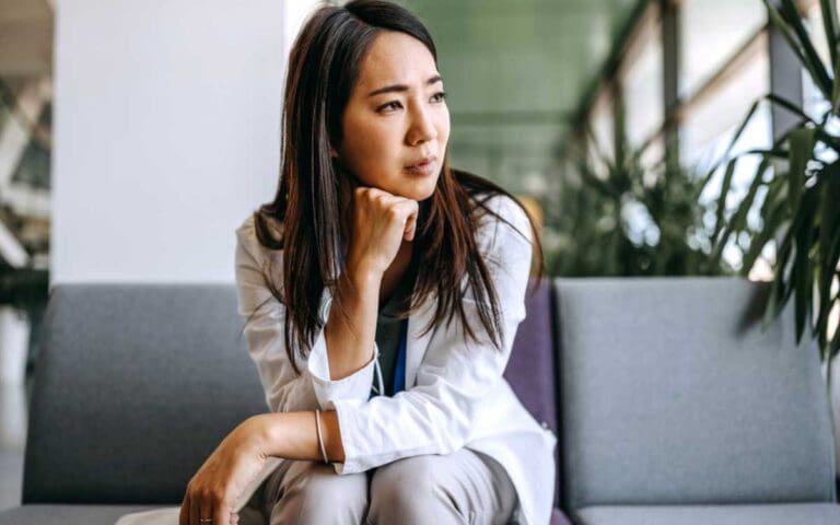 Asian woman with brown hair, wearing a grey suit looking worried, imposter syndrome concept