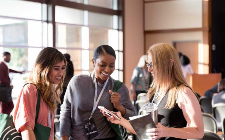 Diverse women attending expo smile at smart phone photos, women in tech networking