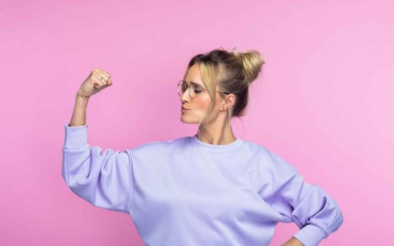 Confident, mid-adult woman flexing her muscles on a pink background, forcing change concept